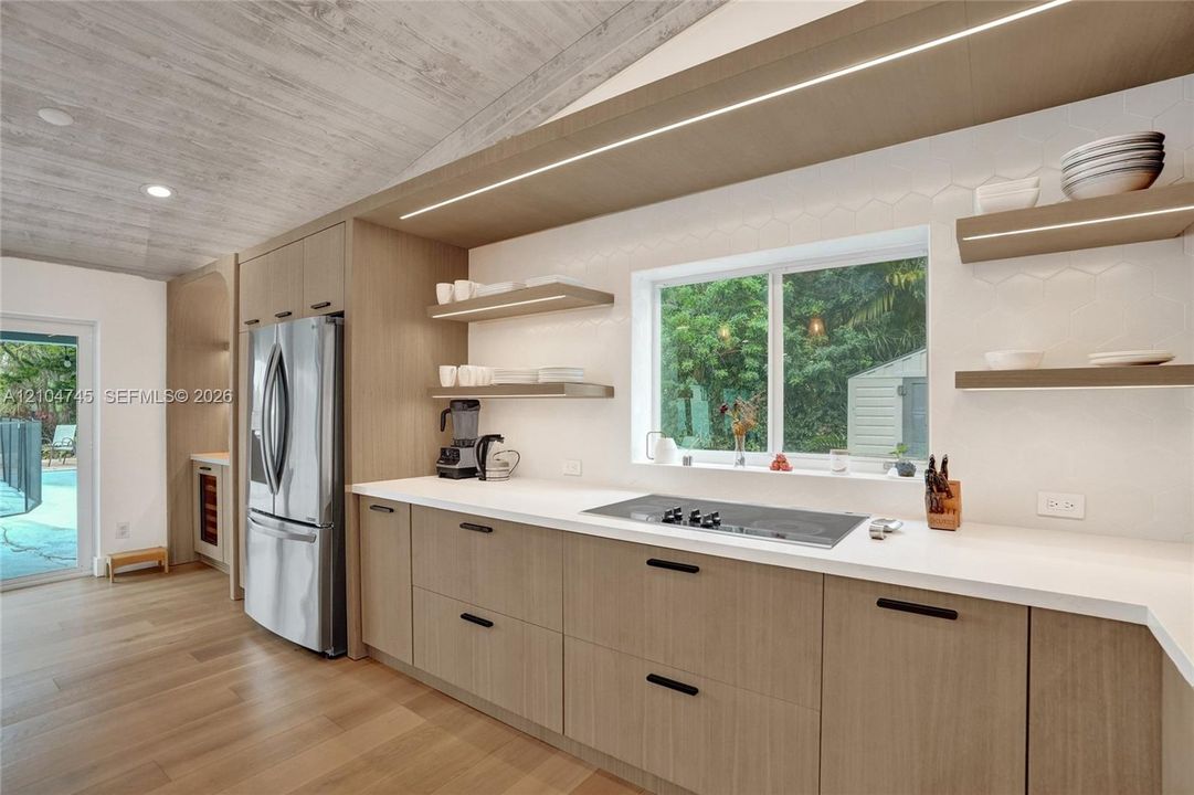 Vaulted wood-finish ceiling, light wood-finish cabinetry, stainless steel appliances, integrated cooktop, and light countertops