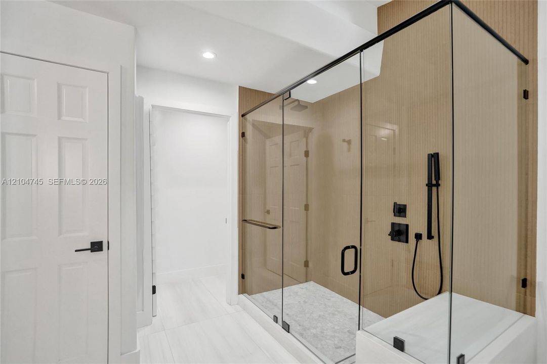 Glass-enclosed shower with matte black fixtures, integrated shower bench, and white tile flooring