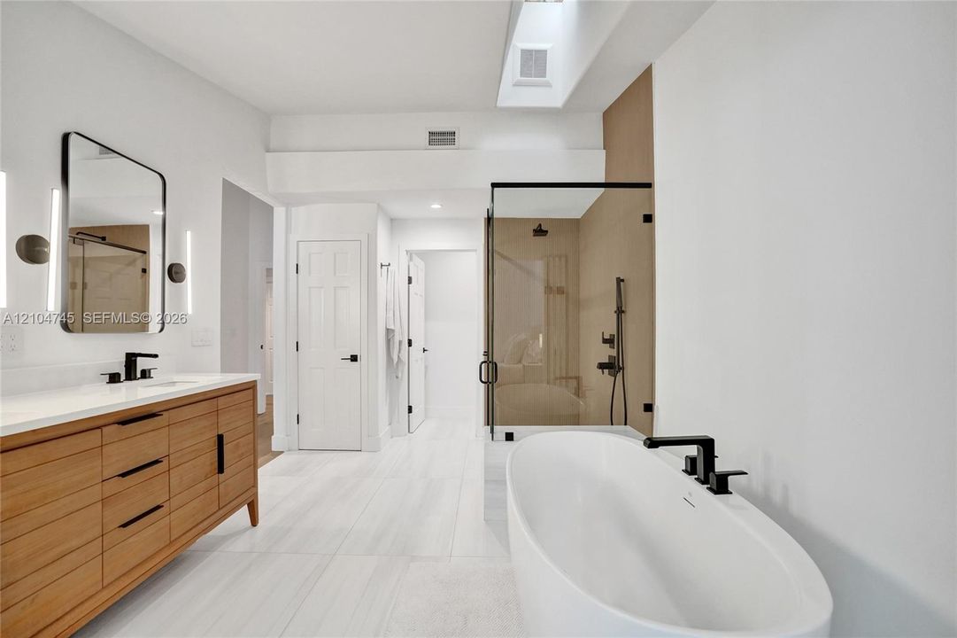 Freestanding soaking tub, frameless glass shower enclosure, wood-finish vanity with countertop, rectangular mirror, and a skylight