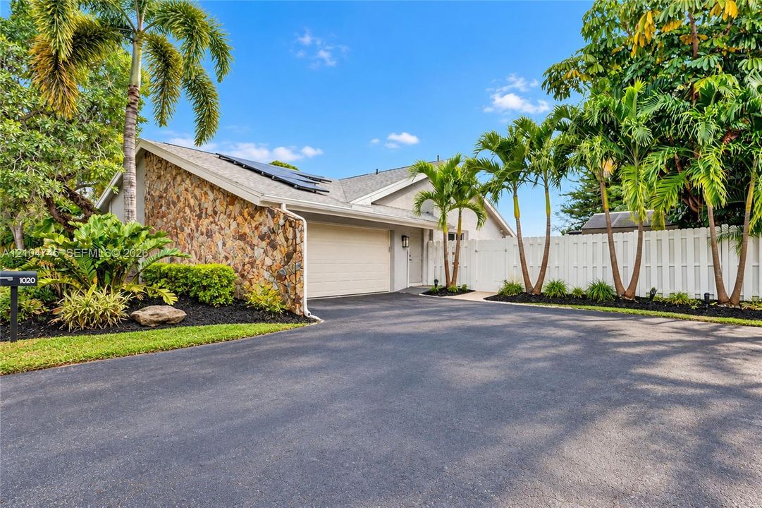 Stone-clad exterior accent, attached garage, well-maintained landscaping, solar panels, and white privacy fencing