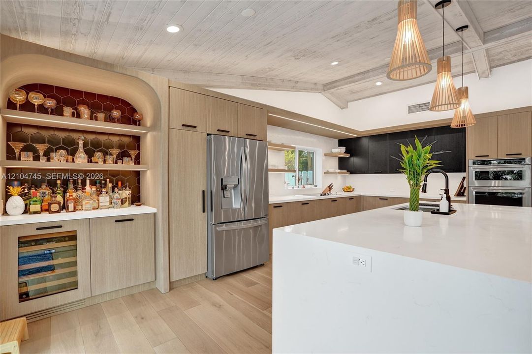 Kitchen featuring wood-finish flooring, white vaulted ceiling with exposed beams, light wood-finish cabinetry, a large kitchen island with a white countertop, and integrated stainless steel appliances