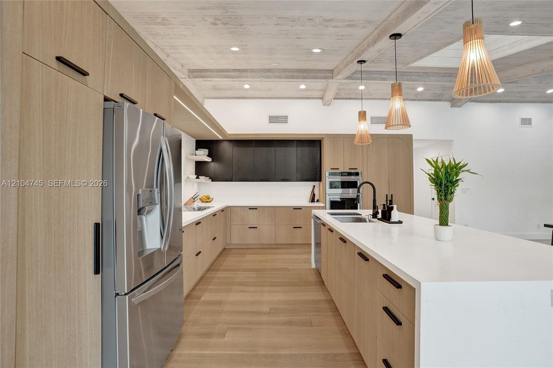 Spacious kitchen featuring light wood-finish cabinetry, stainless steel appliances, a large center island with a sink, white countertops, and wood-finish flooring