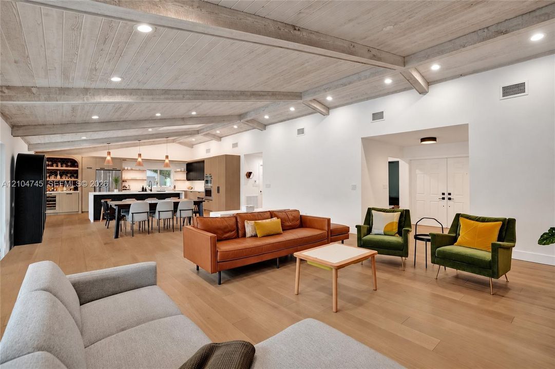 Vaulted ceiling with exposed beams, recessed lighting, wood-finish flooring, built-in kitchen cabinetry, and a large kitchen island with seating