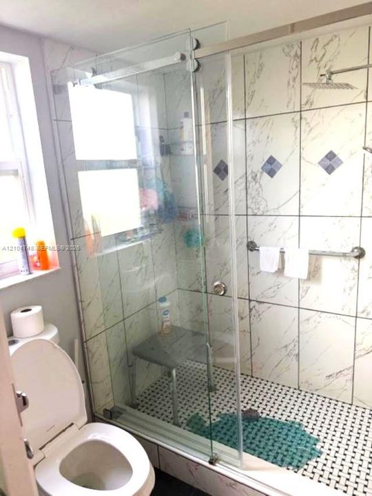 Glass-enclosed shower with white tiled walls, black and white mosaic floor, and a built-in shower seat