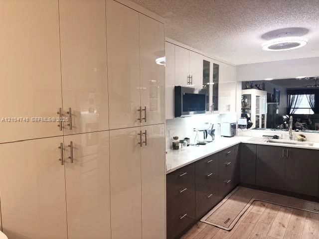 Kitchen featuring extensive light-toned cabinetry with T-bar pulls, wood-finish flooring, a white countertop, and a built-in sink