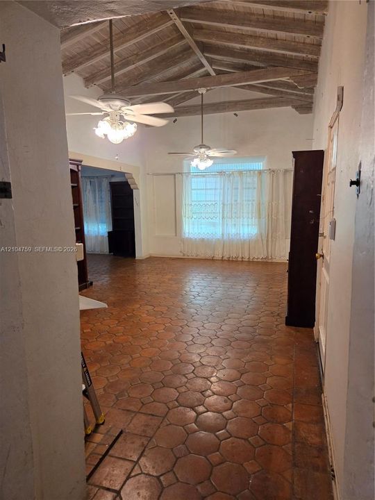 Vaulted ceiling with exposed wood beams, octagonal terracotta tile flooring, and dual ceiling fans with integrated lighting
