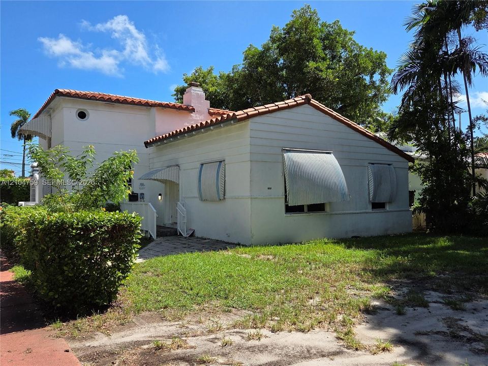 Spanish Colonial architecture featuring a clay tile roof, light-toned exterior finish, and metal window awnings