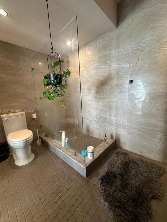 Walk-in shower with clear glass enclosure and stone tile surround