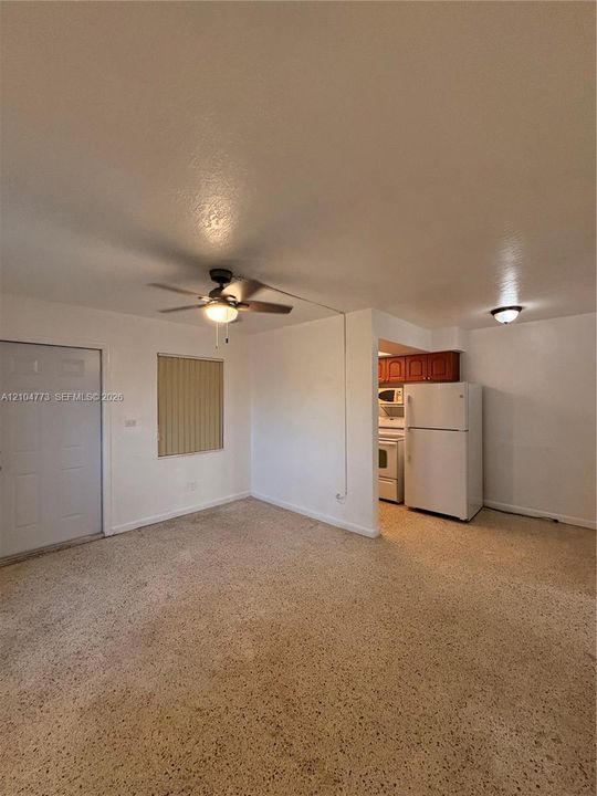 Textured flooring, a ceiling fan with integrated lighting, and a window with horizontal blinds