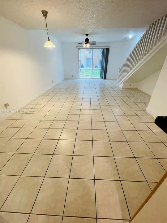 Open-concept room featuring neutral ceramic tile flooring, a staircase with a wooden balustrade, a ceiling fan, and sliding glass doors