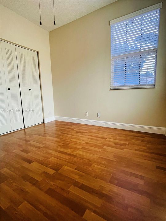 Wood-finish flooring, high ceilings, dual louvered closet doors, and a window fitted with horizontal blinds