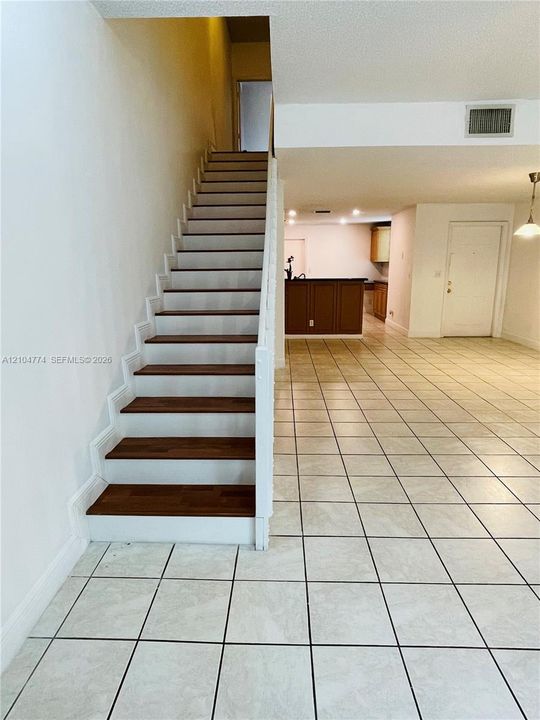 Staircase featuring wood-finish treads and white risers, square ceramic tile flooring, and a kitchen peninsula with dark-toned cabinetry