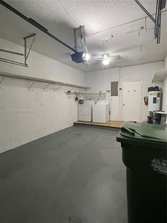 Attached garage featuring a painted concrete floor, built-in wall shelving, and dedicated laundry area with overhead lighting