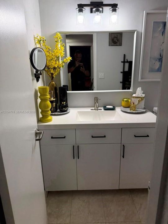 White vanity featuring a built-in sink, dark hardware, and a framed mirror