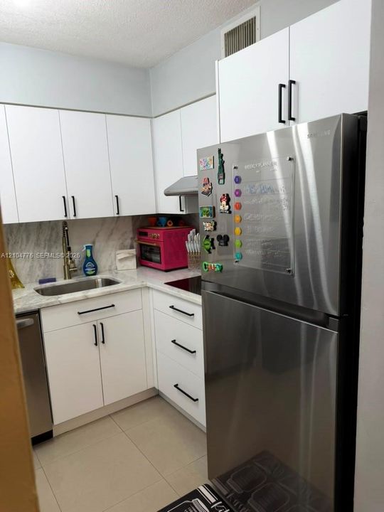 White cabinetry with matte black hardware, stainless steel appliances, granite-style countertops, and a tile backsplash