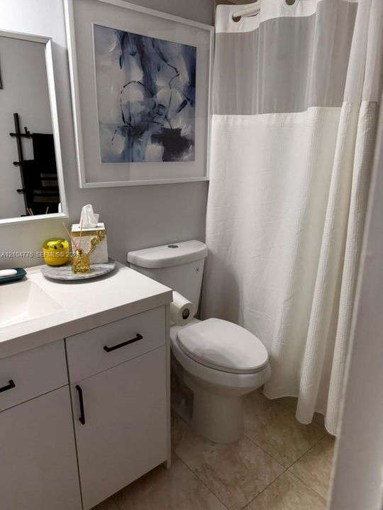 Vanity with integrated sink and matte black hardware, white toilet, and neutral tone tile flooring