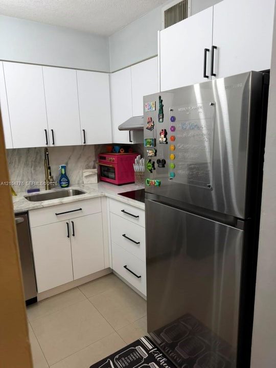 Modern kitchen featuring white cabinetry, stainless steel appliances, a built-in cooktop, and a stainless steel sink