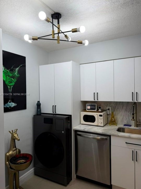 Modern sputnik-style ceiling light fixture, white upper and lower cabinetry, stainless steel dishwasher, and a stone backsplash