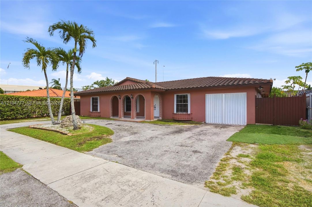 Exterior featuring a tile roof, arched entryway, a paved driveway, and mature palm trees