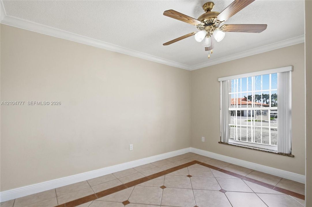 Tile flooring with a decorative inlay, crown molding, and a ceiling fan with integrated lighting