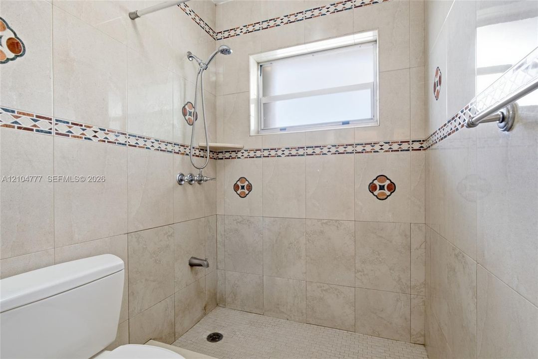 Tile-surrounded shower with a built-in shower niche, mosaic tile accents, and a window for natural light