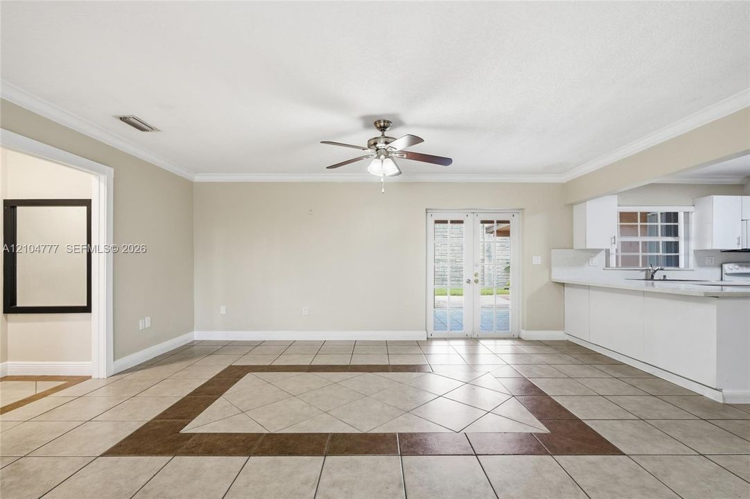 Spacious living area featuring tile flooring with a decorative inlay, a ceiling fan, and crown molding