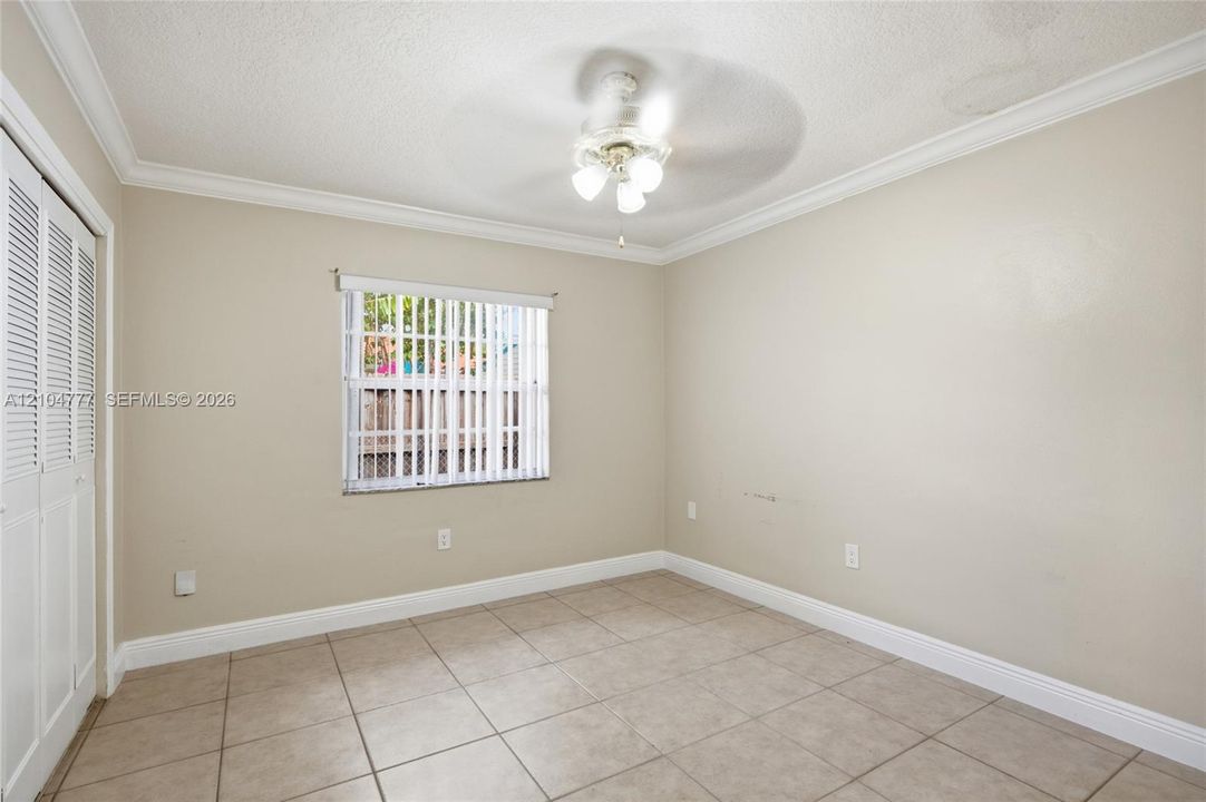Neutral tone walls, crown molding, ceiling fan with integrated lighting, tiled flooring, and louvered closet doors