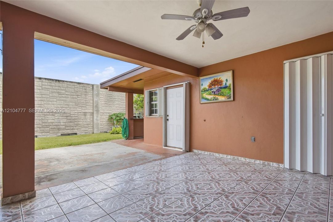 Covered patio featuring patterned tile flooring, a ceiling fan with light, and a privacy wall