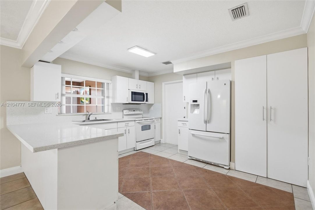 White cabinetry and appliances, solid surface countertops, tile flooring, and a built-in microwave