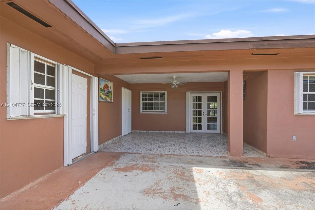 Covered patio with integrated ceiling fan, French doors, and windows featuring accordion shutters
