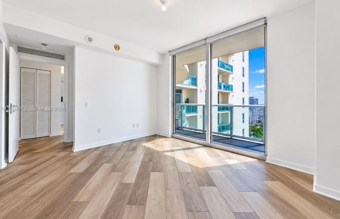 Wood-finish flooring with white walls and a full-height glass sliding door with roller shades