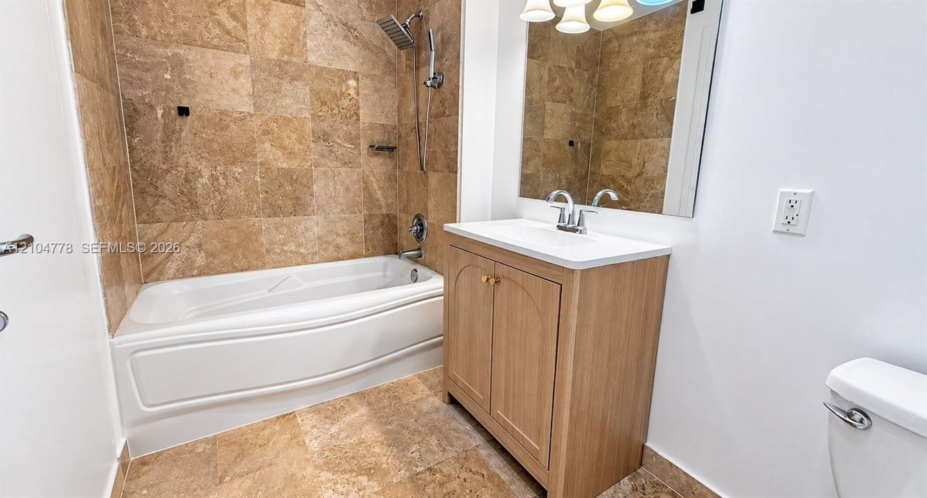 Bathroom featuring a white bathtub, tiled shower surround, wood-finish vanity with countertop, and wall-mounted mirror