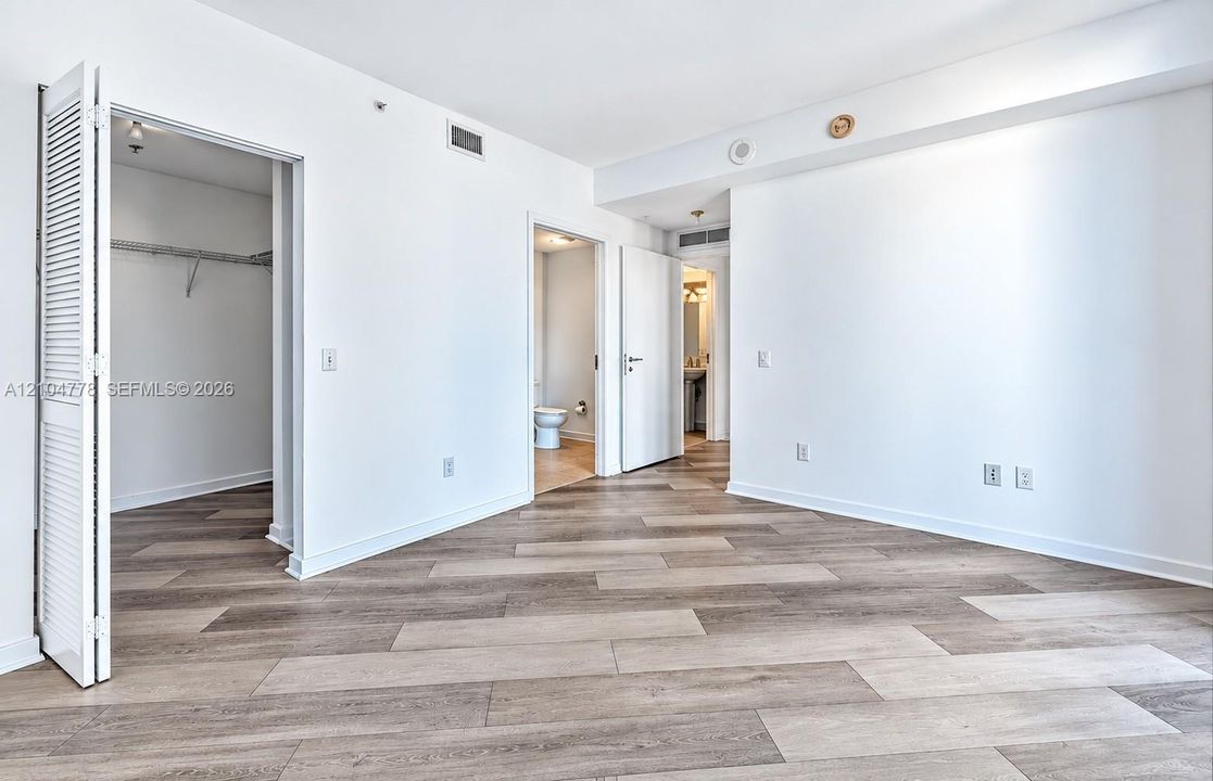 Wood-finish flooring throughout, white walls, louvered closet door, recessed lighting, and a bathroom access door