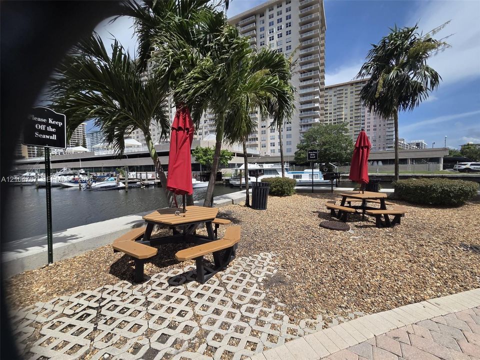 Waterfront grounds featuring a seawall, gravel landscaping, mature palm trees, and integrated concrete pavers