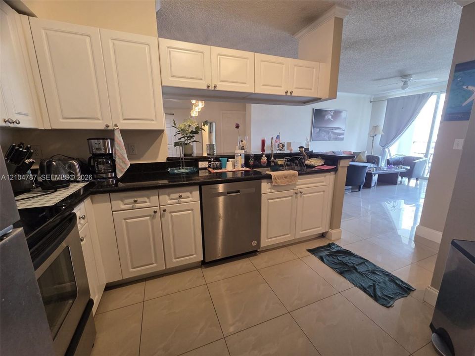 Kitchen featuring white cabinetry, dark stone-finish countertops, stainless steel dishwasher, stainless steel range, and tile flooring