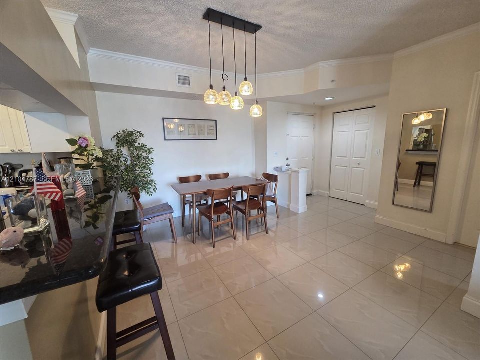Open-concept dining area featuring polished tile flooring, a multi-pendant light fixture, and a dark stone breakfast bar