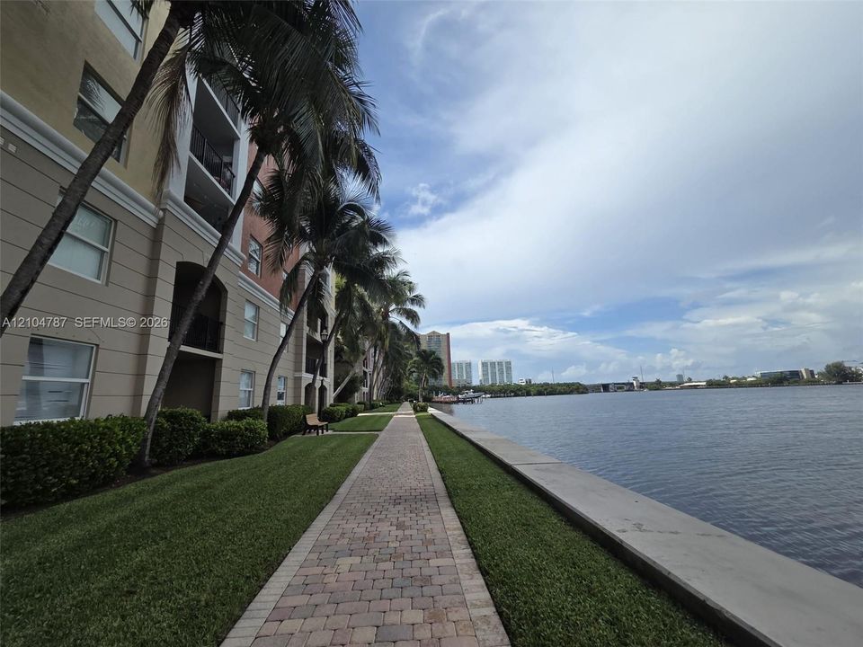Waterfront walkway featuring paver-style hardscaping, manicured grass borders, and mature palm trees