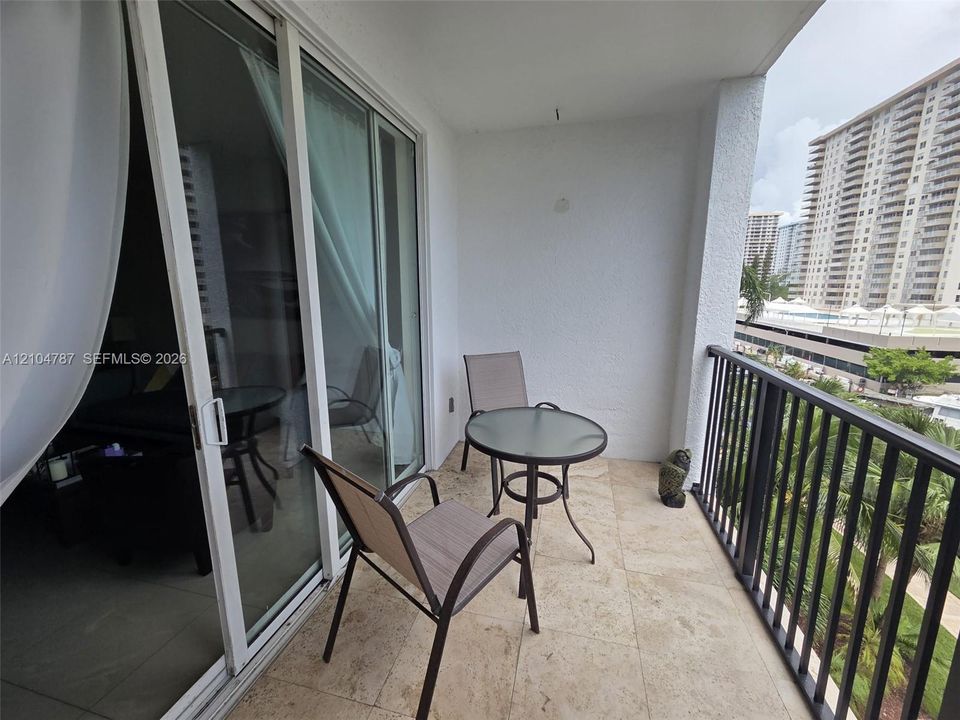 Covered balcony featuring stone-tiled flooring, white stucco walls, and black metal railings with vertical balusters