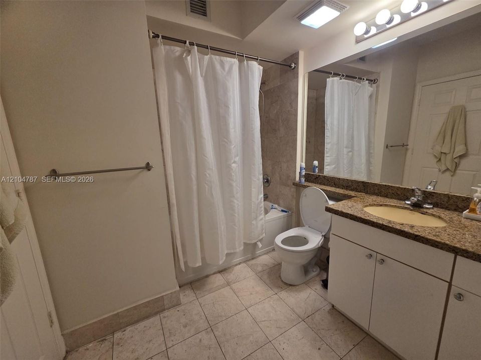 Full bathroom featuring stone-tiled flooring, stone-surfaced vanity with integrated sink, expansive wall-mounted mirror, and tile-surround shower combination