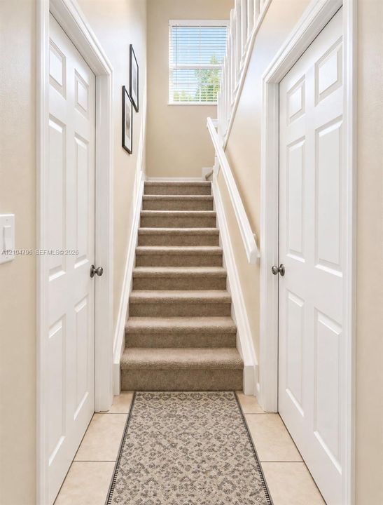 Staircase featuring carpeted steps, a white painted railing, neutral wall finishes, and a window providing natural light