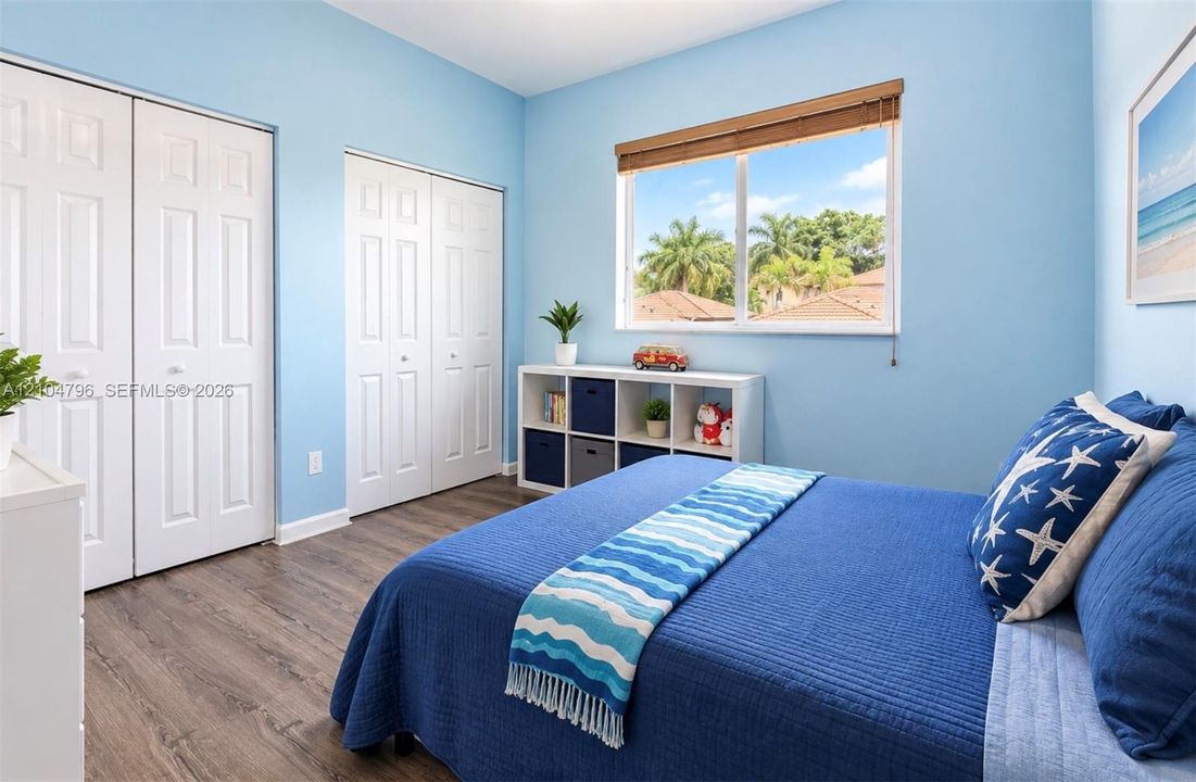 Room featuring wood-finish flooring, dual-door closets, and a window with wood-slat blinds