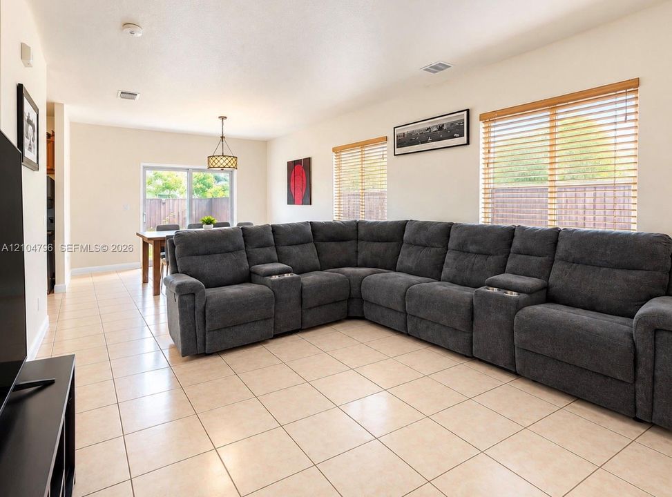 Open-concept interior featuring large-format ceramic tile flooring, multiple windows with horizontal blinds, and a hanging drum pendant light fixture