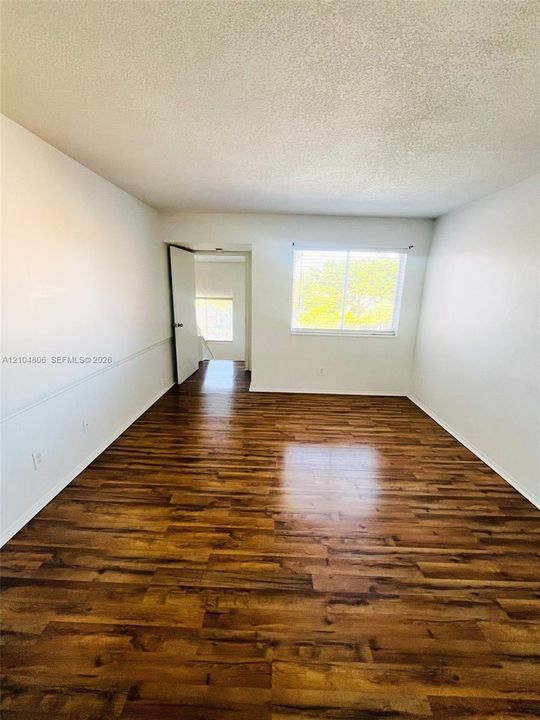 Wood-finish flooring, white wall paneling, and a large window with horizontal blinds
