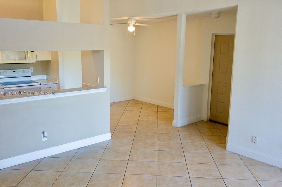 Open concept layout with neutral tile flooring, a kitchen pass-through, a ceiling fan, and a light-toned interior door
