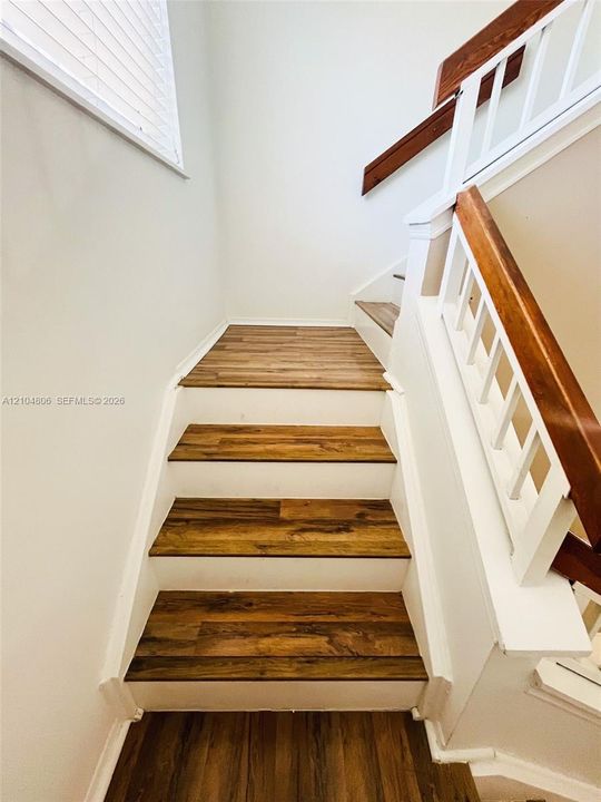 Staircase featuring wood-finish treads, white risers, and a matching handrail with white balusters