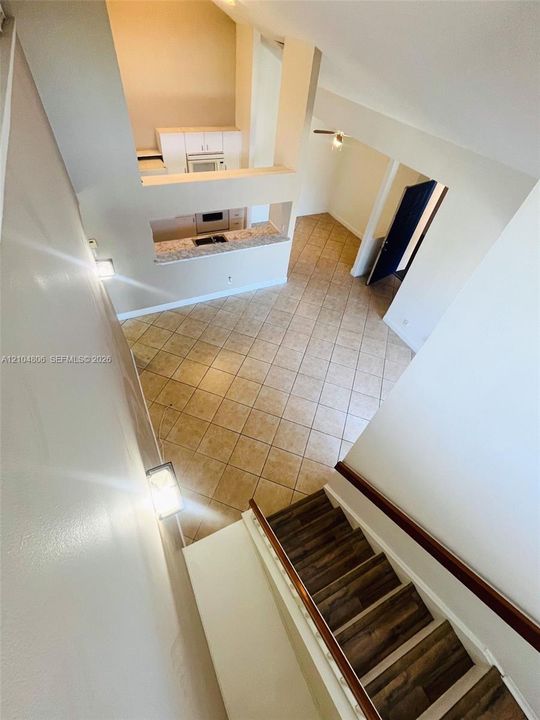 Two-story living space featuring a wood-finish staircase, tiled flooring, vaulted ceilings, a kitchen with built-in appliances, and a breakfast bar with stone-finish countertops