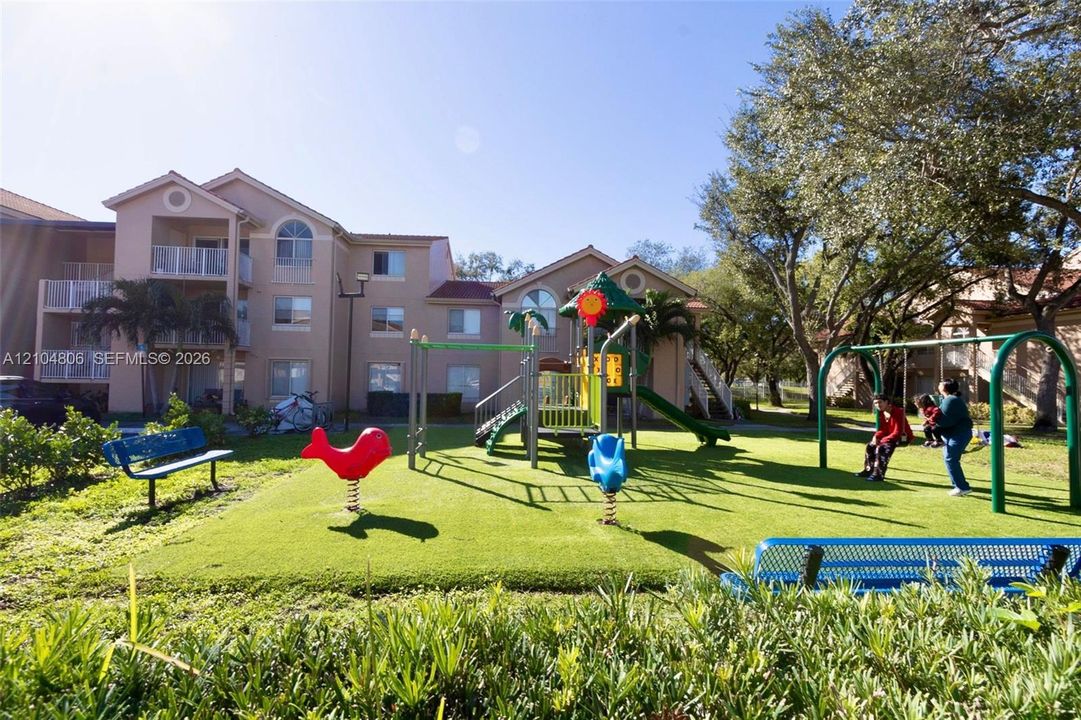 Outdoor playground featuring a swing set, slide structure, and spring riders on a green turf surface
