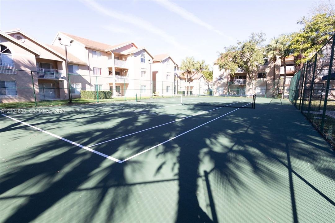 Full-size tennis court with a dark green playing surface and white boundary lines