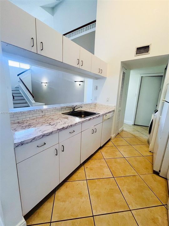 Kitchenette with white cabinetry and dark hardware, stone-finish countertops, ceramic tile backsplash, and a stainless steel sink