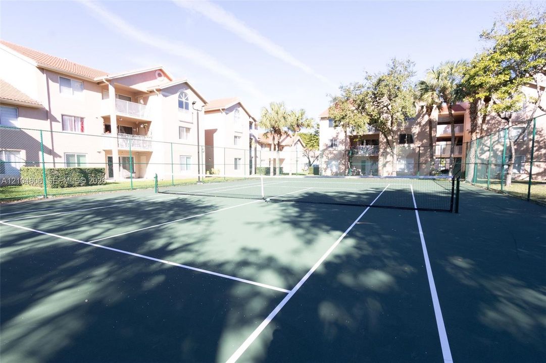 Tennis court with dark green surfacing and white lines, surrounded by fencing